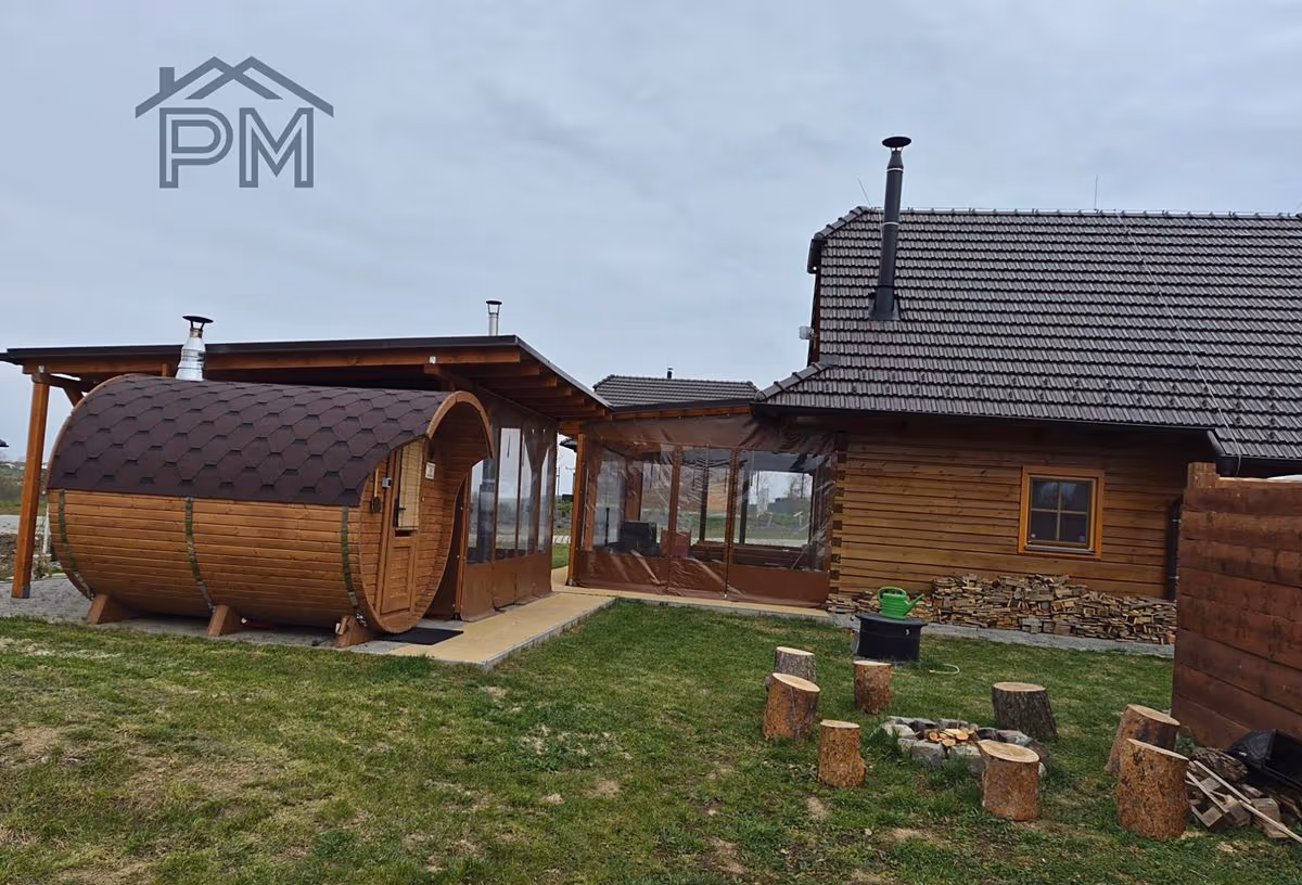 Sudová sauna pod přístřeškem vedle kryté terasy, před domem ohniště a zásoba dřeva