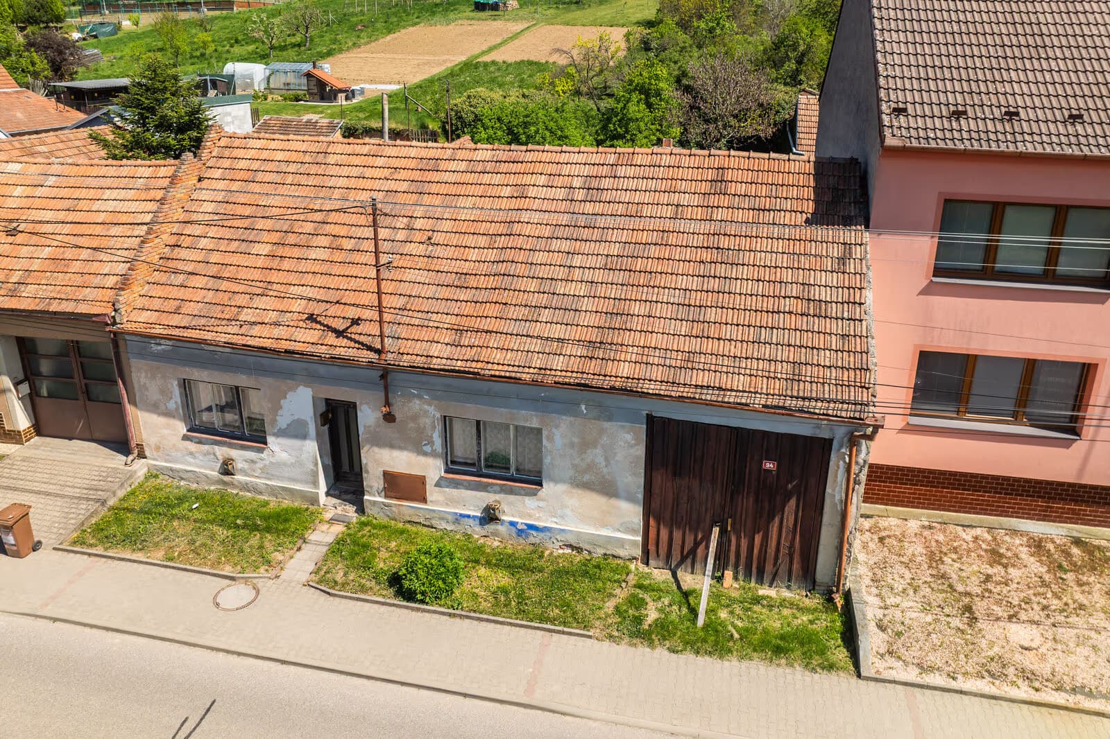 Letecký pohled na nemovitost shora — červená tašková střecha, uliční průčelí s chodníkem, dřevěná vrata č. 94 a část zahrady za domem