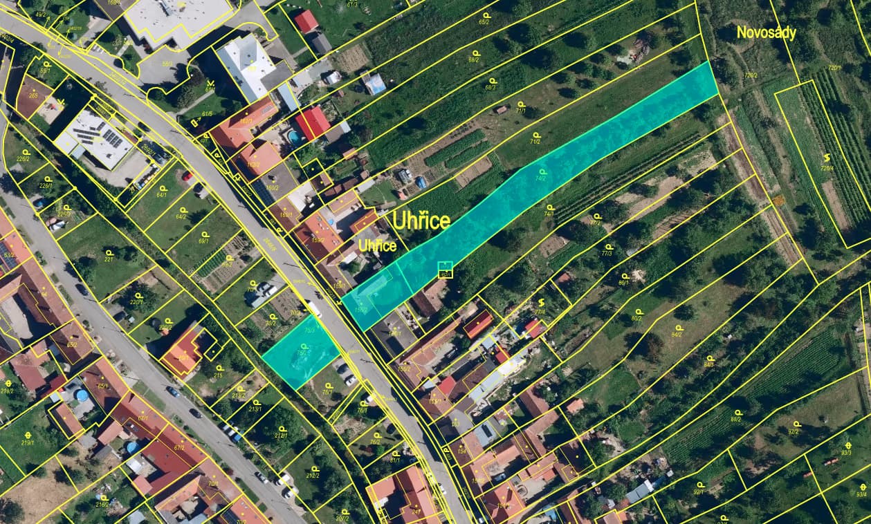 Katastrální mapa s tyrkysově zvýrazněnými parcelami pozemku — protáhlý pás od ulice do zahrad a parcela naproti přes silnici, žluté hranice parcel s čísly