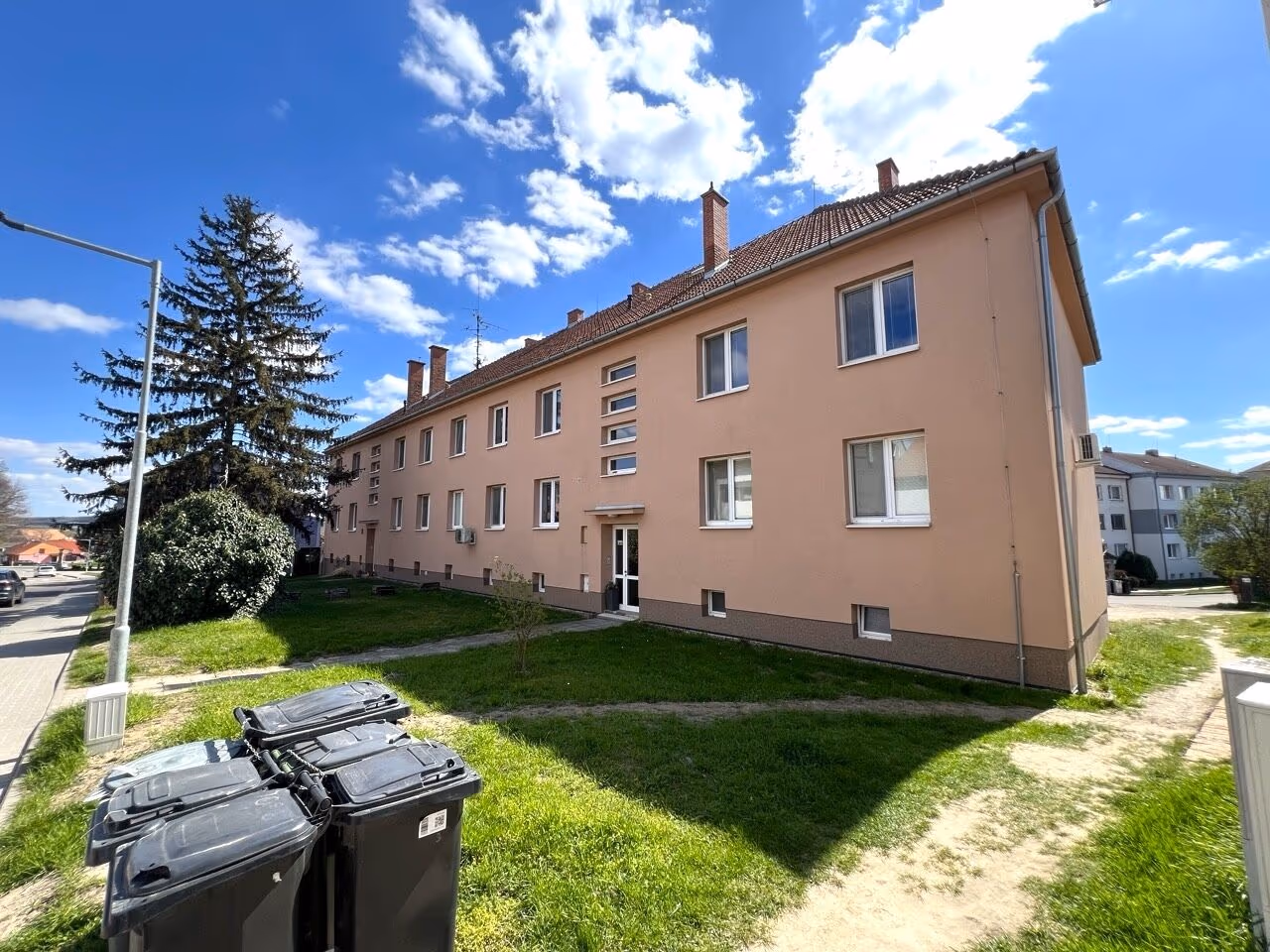 Třípatrový bytový dům s meruňkovou fasádou a trávníkem před domem, Drnholec