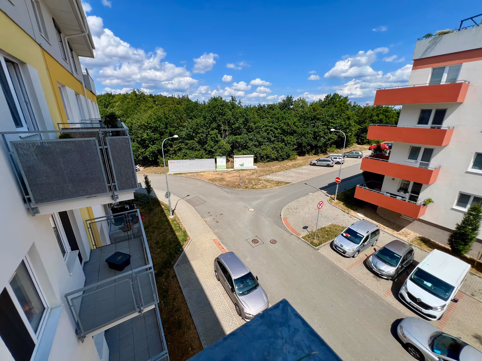 Výhled z balkonu na křižovatku, parkování a lesík na okraji sídliště