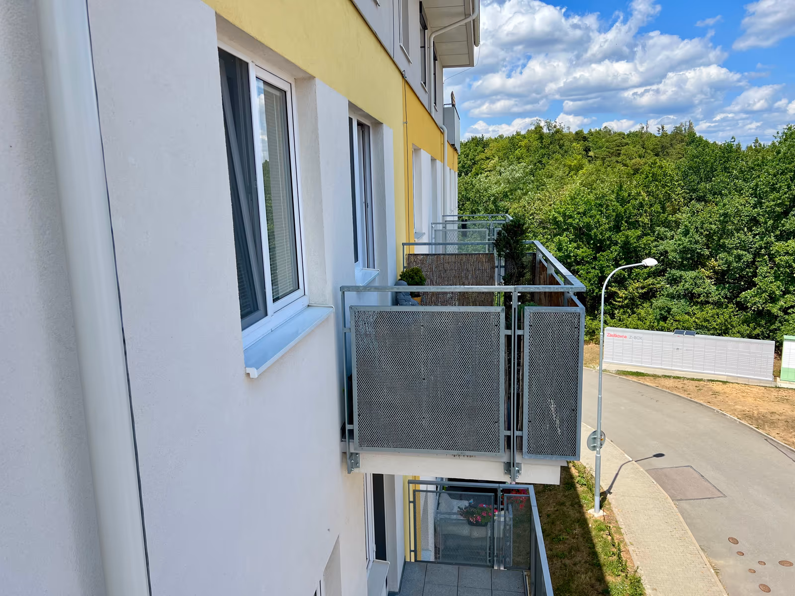 Boční pohled na dům s balkony a lesem v pozadí