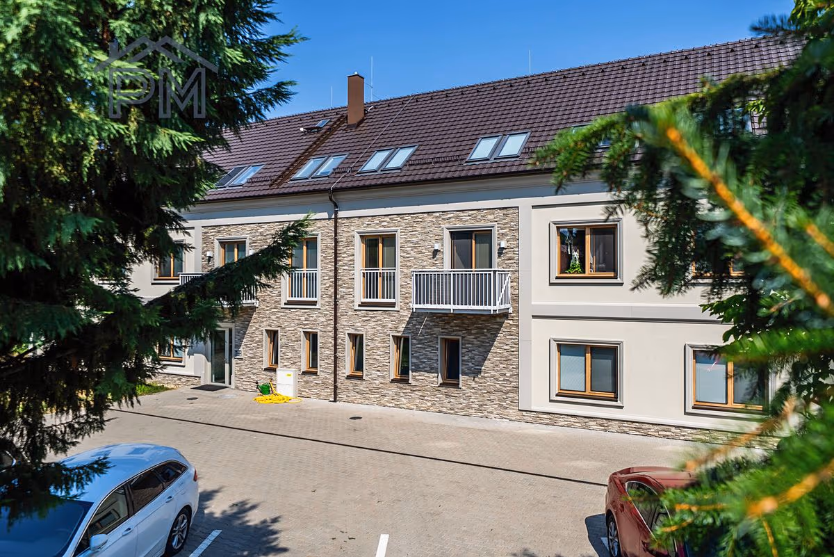 Bytový dům od parkoviště, v popředí vzrostlé jehličnany
