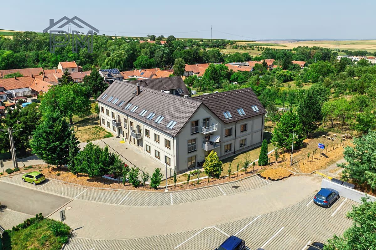 Letecký pohled na dům a parkoviště, v pozadí obec a pole