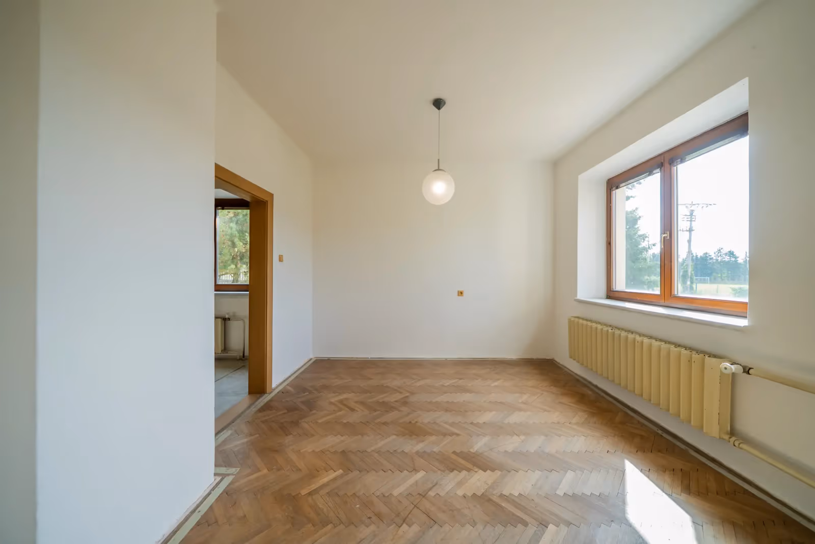 Pokoj v přízemí s parketami a oknem směrem ke hřišti