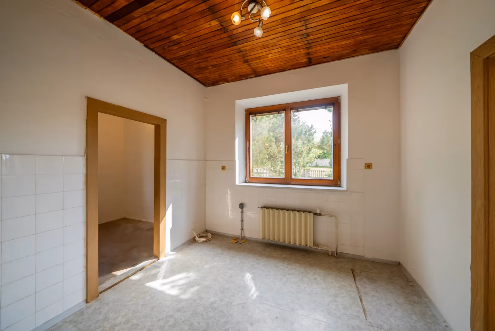 Kuchyně s dřevěným palubkovým stropem, bílými obklady a oknem do zahrady; vedle spíž