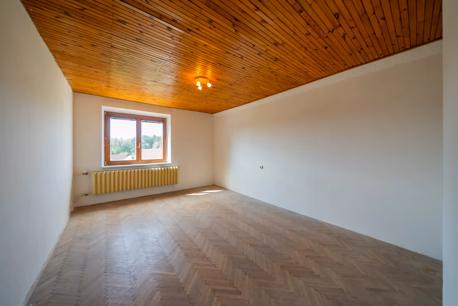 Pokoj v patře s dřevěným palubkovým stropem a parketami